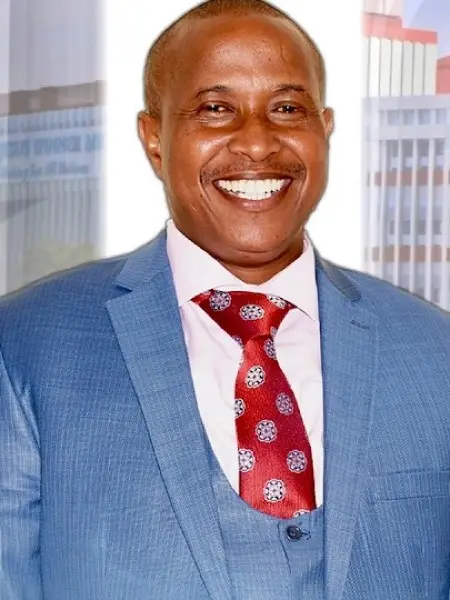 Bishop Edward Mwai smiling, in a blue suit and red patterned tie
