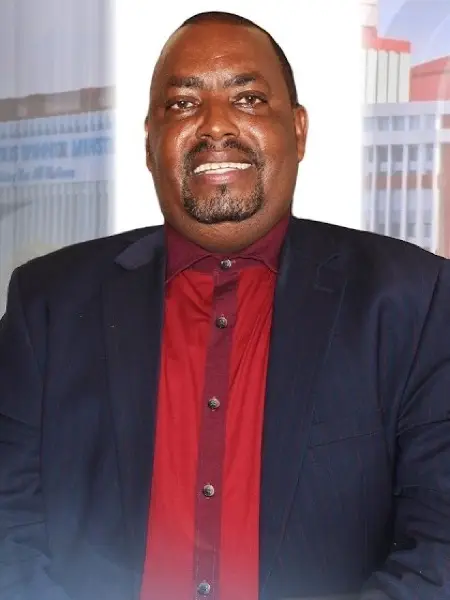 Rev. Raphael Mwiti smiling, in a navy suit and red shirt