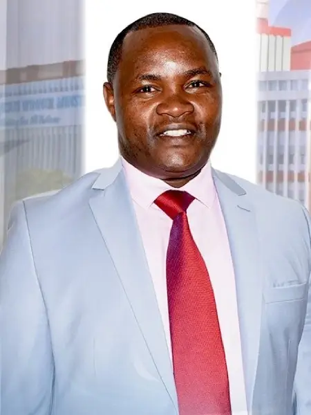 Rev. Justus Muriithi smiling, in a light grey suit and red tie